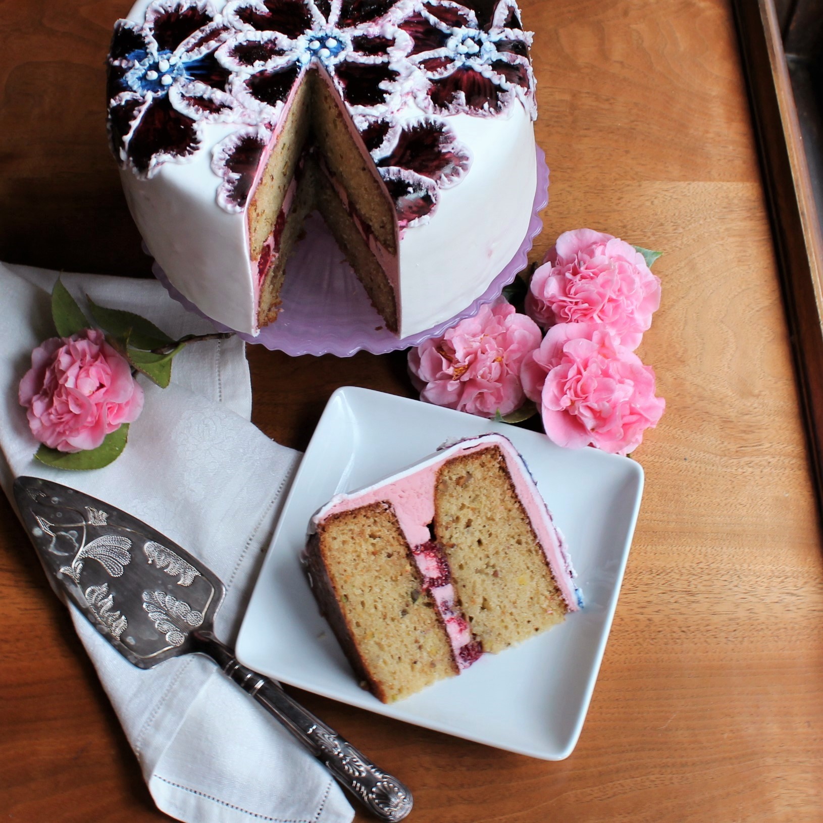 A pistachio cake with raspberry rose frosting on a pink cake stand with a slice on a white plate